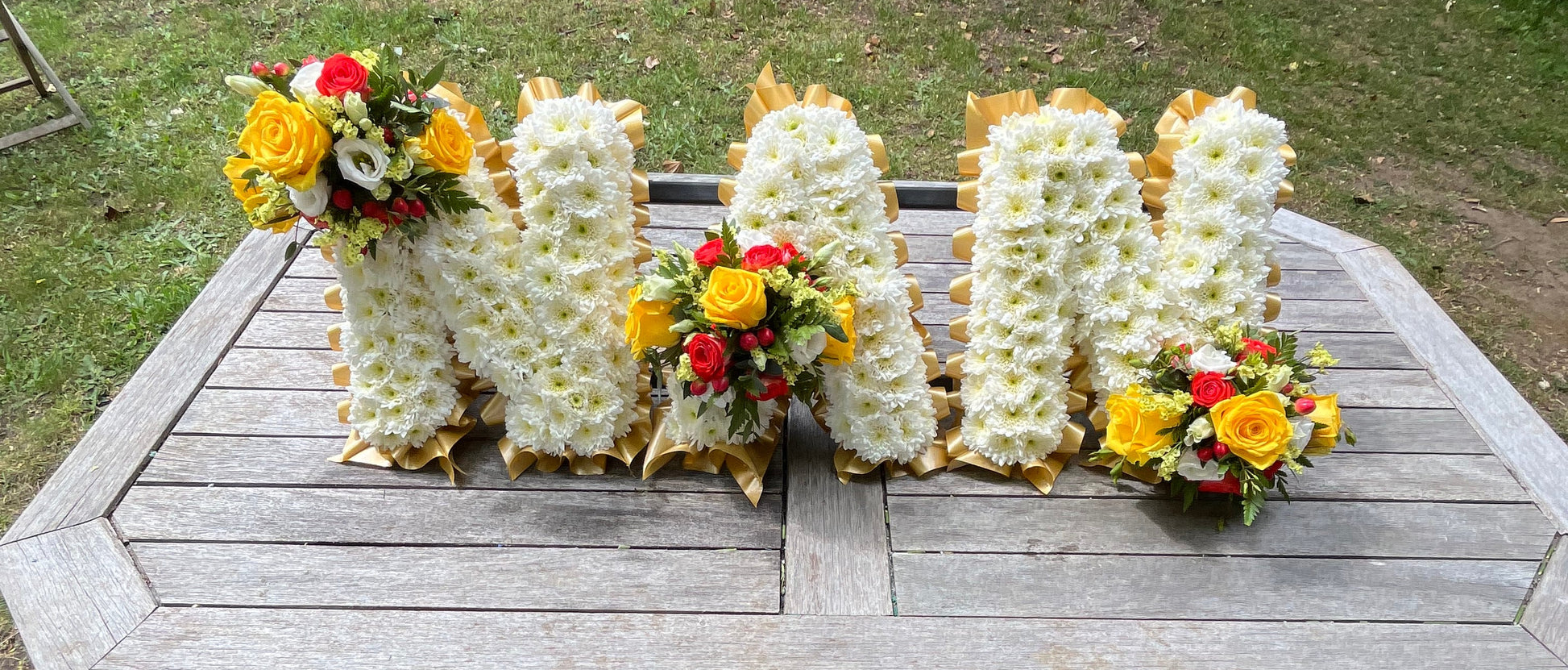 Floral arrangements shaped like letters NAN on a wooden surface outdoors.