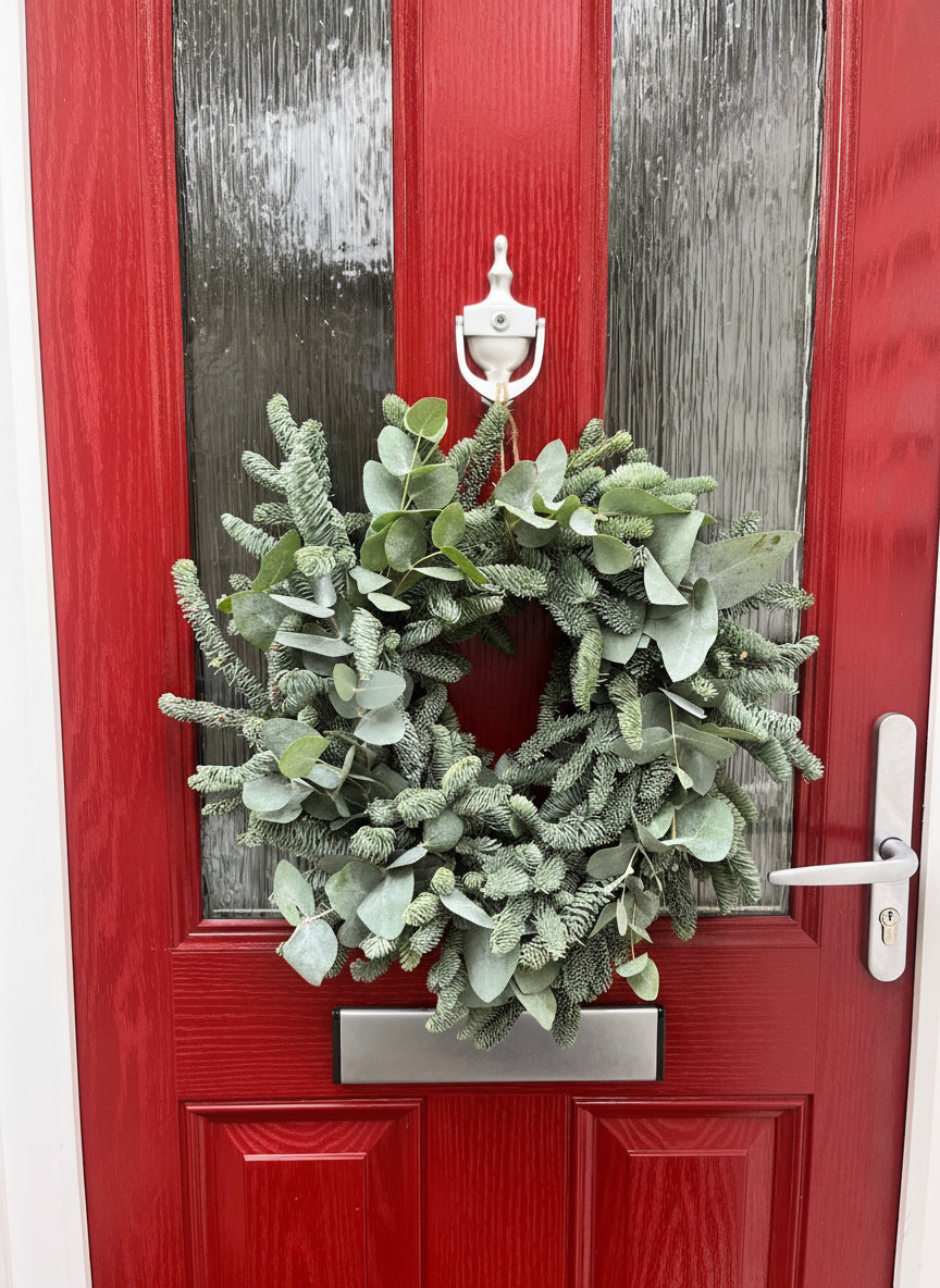 Green wreath on a red door with silver handle and address number.