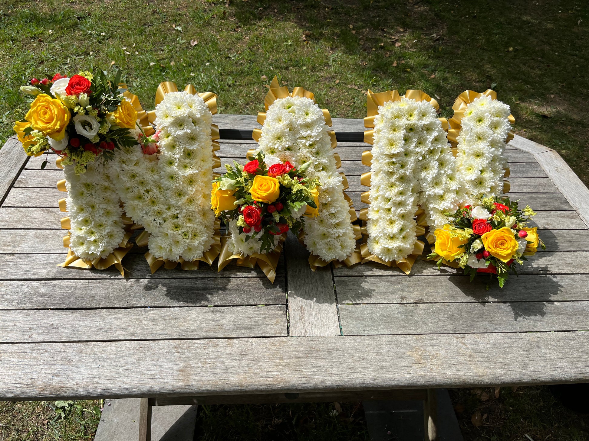 Floral letters spelling 'NAN' on a wooden surface outdoors.