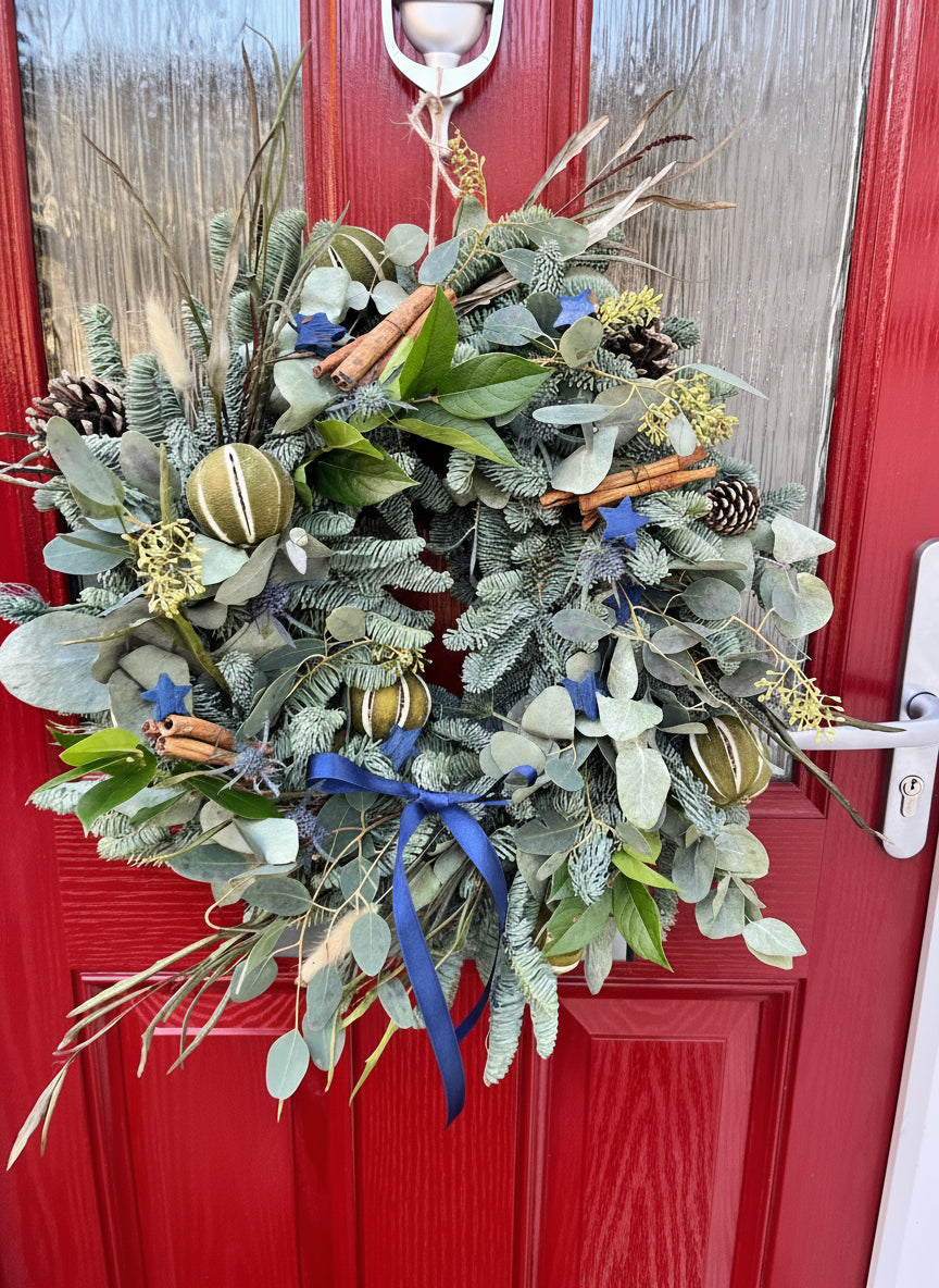 Decorative wreath with greenery and blue ribbons on a red door.