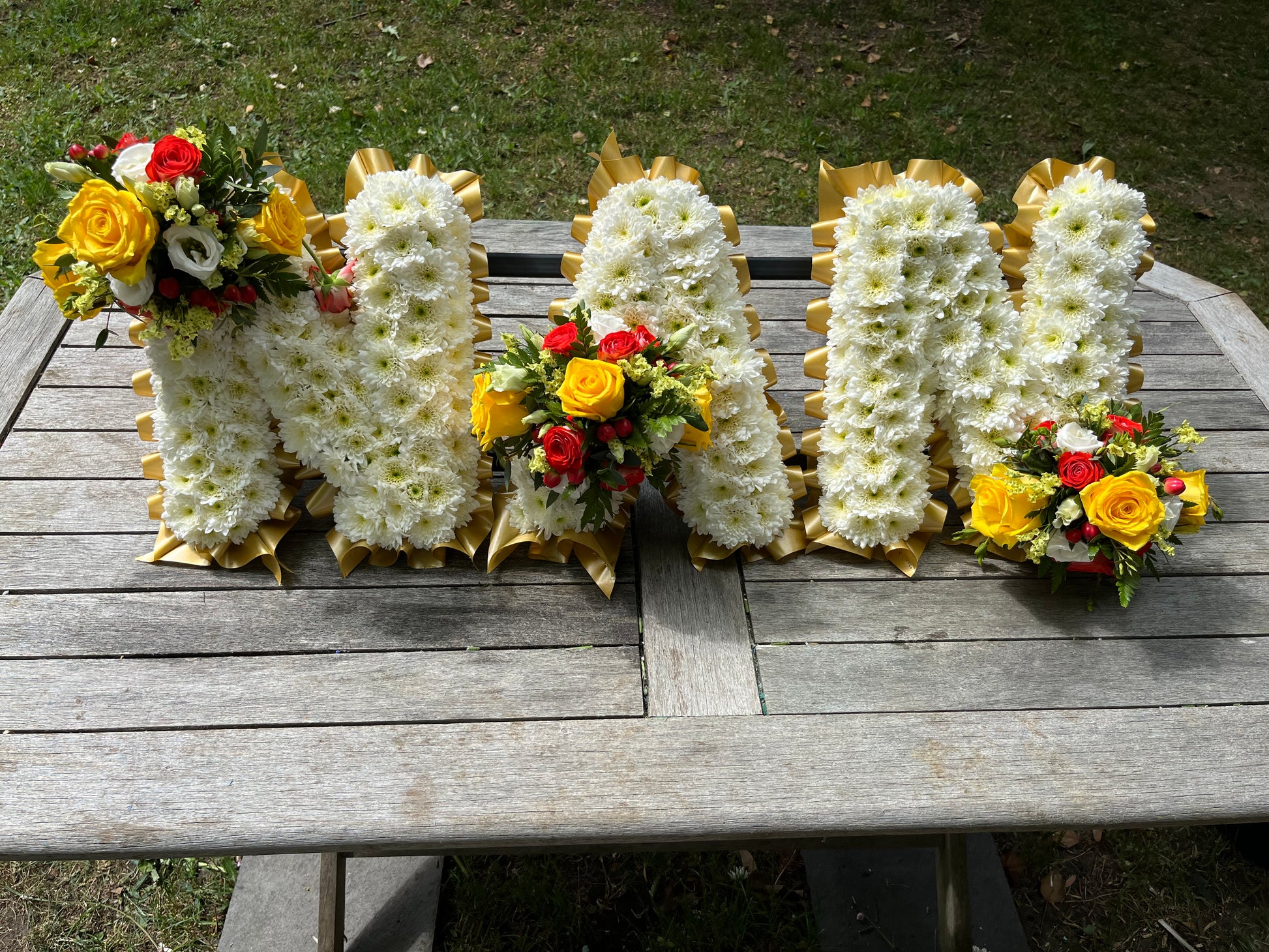 Floral arrangements shaped like letters on a wooden table outdoors.