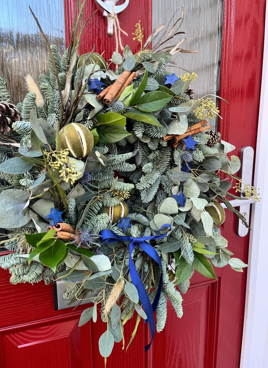 Decorative wreath with greenery, ribbons, and pinecones on a red door.