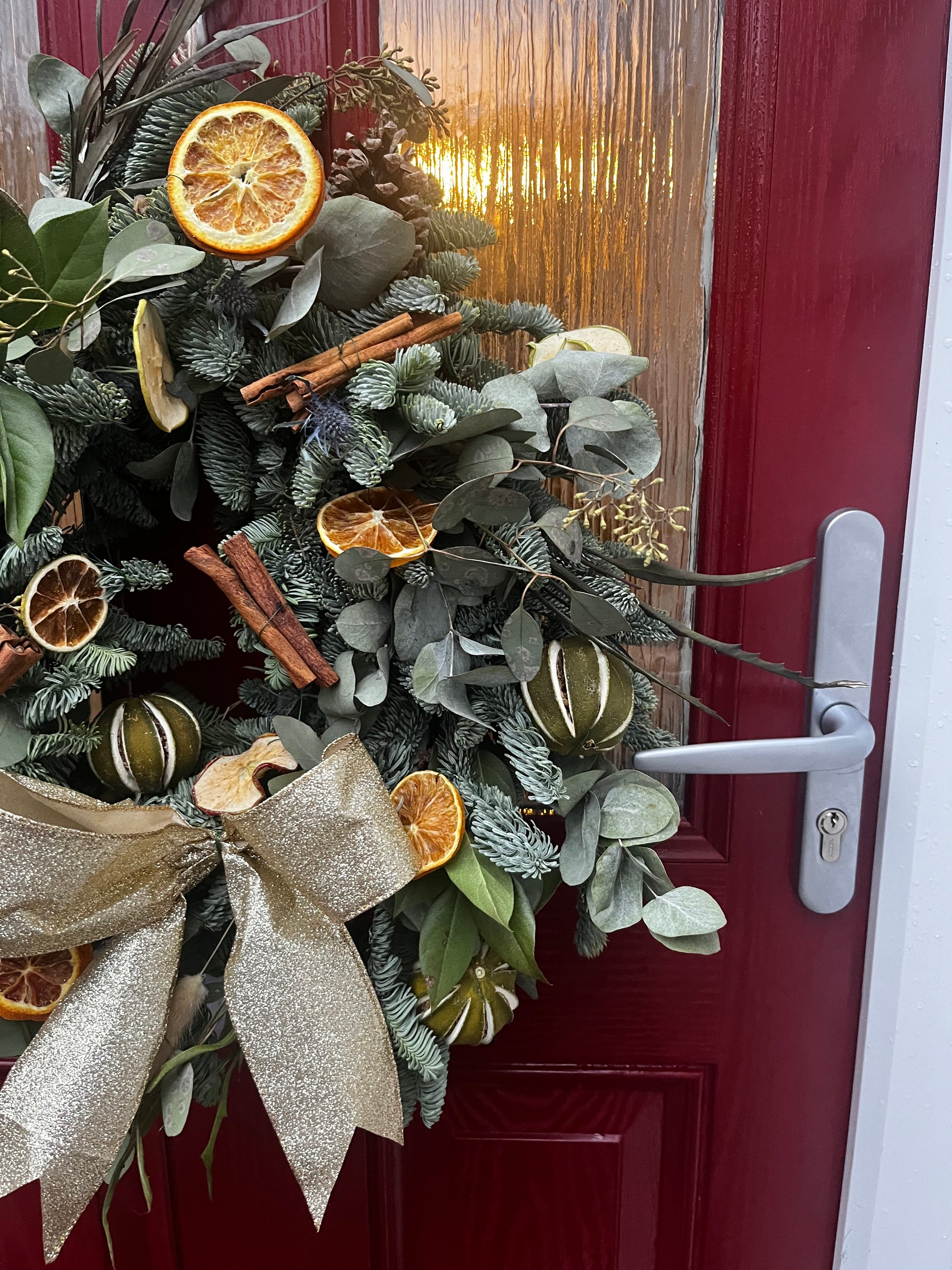 Decorative wreath with greenery, oranges, and a bow on a red door.