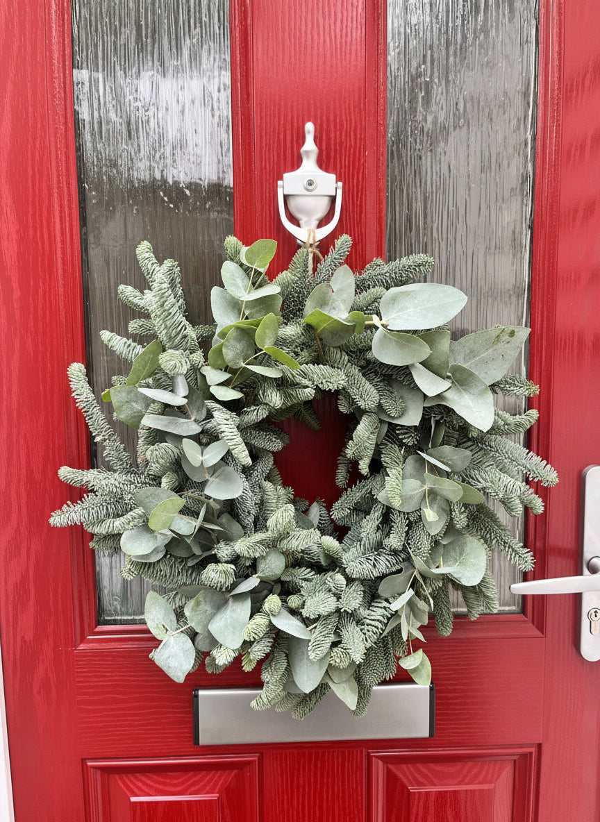 Green wreath on a red door with silver handle and mail slot.