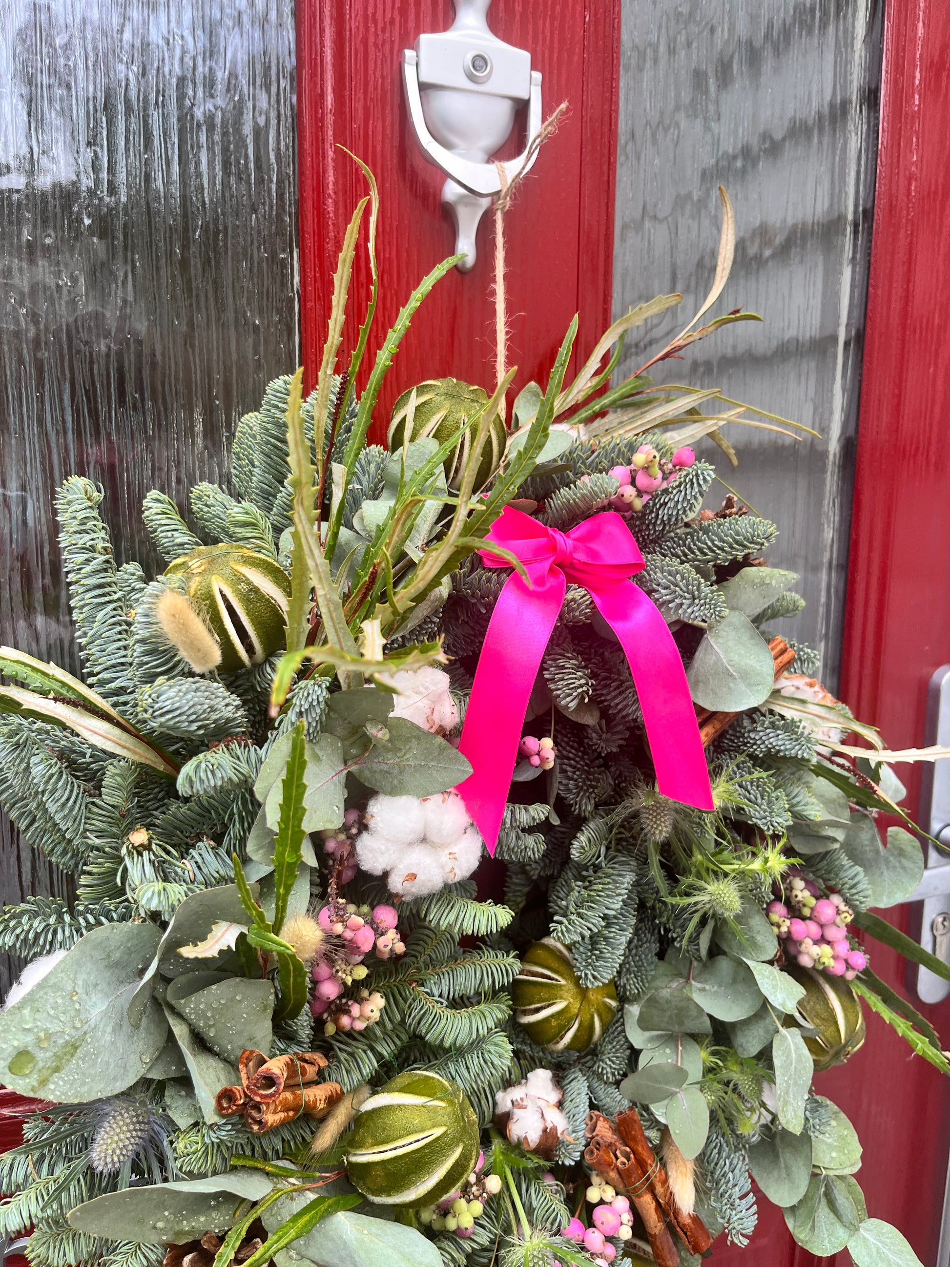 Decorative wreath with greenery, pink ribbon, and small flowers on a wooden surface.