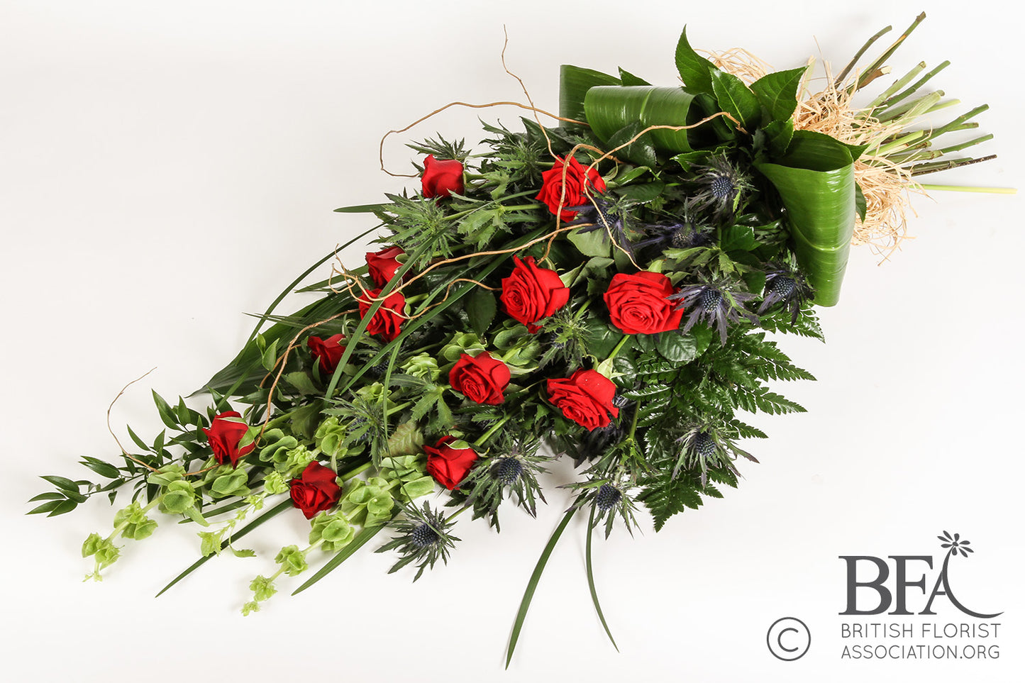 A stunning red rose sheaf, featuring long-stemmed red roses and mixed foliage, thoughtfully crafted in Stevenage as a beautiful and elegant tribute.