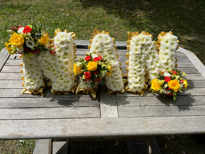 Floral letters spelling 'NAN' on a wooden surface outdoors.