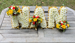 Floral arrangements shaped like letters 'NAN' on a wooden surface.