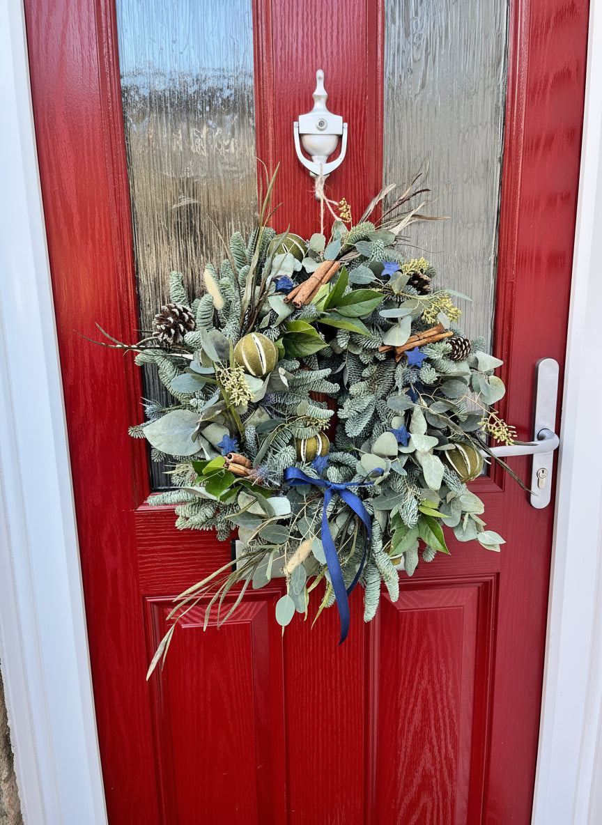 Decorative wreath with greenery and ornaments on a red door.