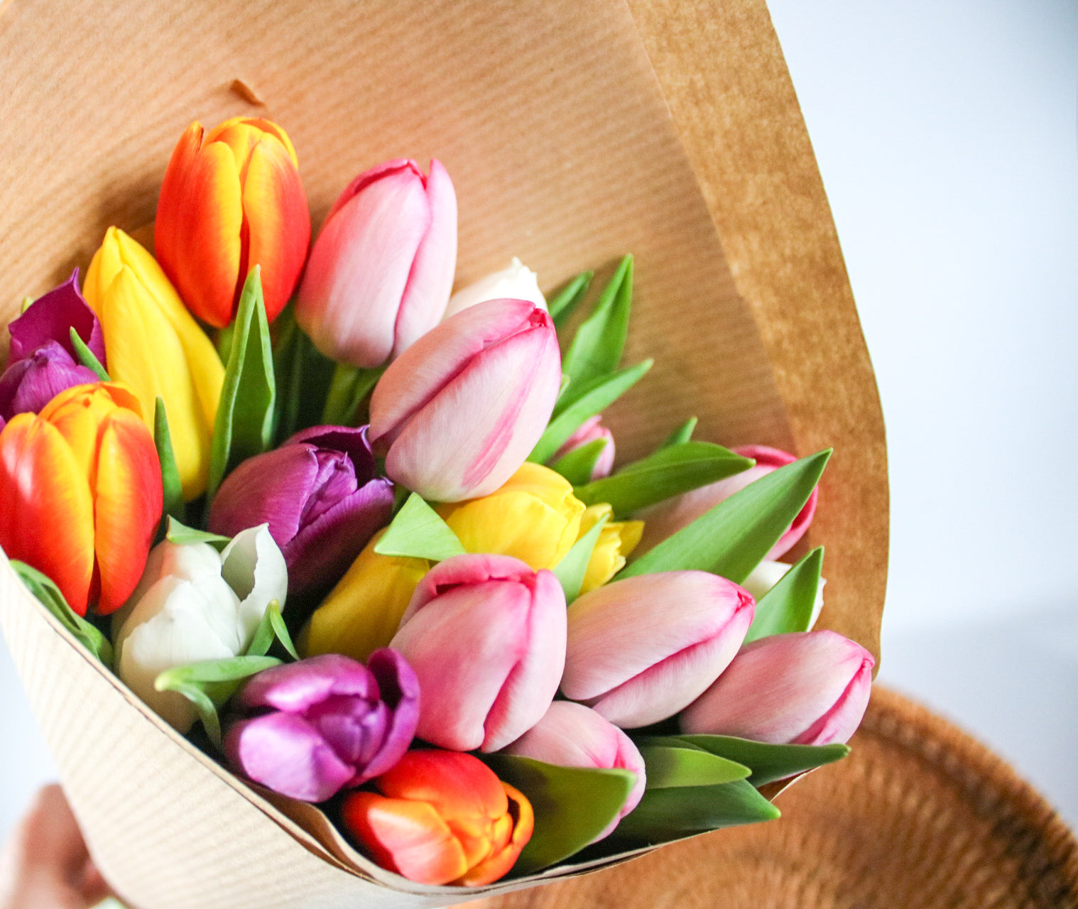 Bouquet of colorful tulips in a woven basket on a light background