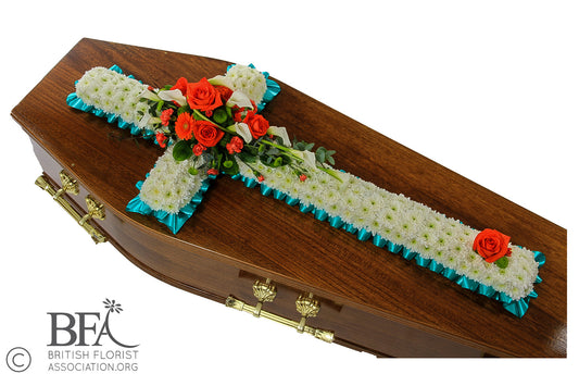A massed cross tribute with chrysanthemums and a selection of orange flowers on top, symbolizing remembrance.