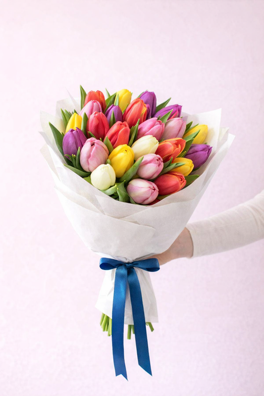 Bouquet of colorful tulips with a blue ribbon held by a person on a light pink background