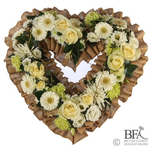 A loose open white heart tribute, crafted with fresh greenery and mixed flowers for a natural and meaningful tribute.