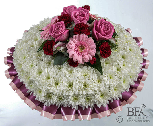 A cushion posy pad in pink and red, featuring white chrysanthemums, pink ribbon, and a red rose posy.

