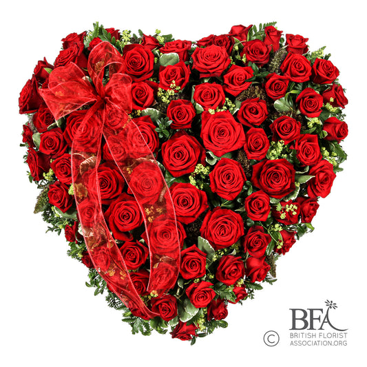 A red rose closed heart tribute, symbolizing love and remembrance, created with seasonal foliage and berries.
